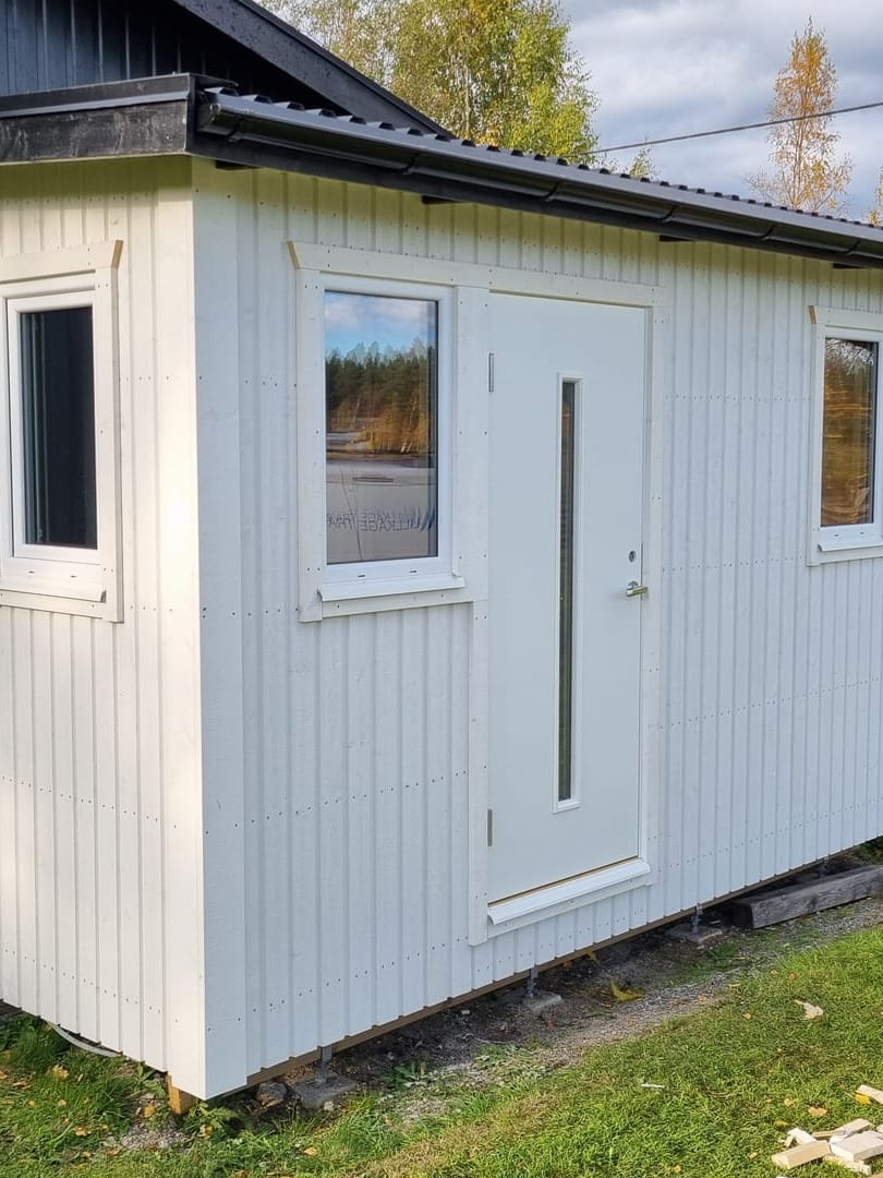 Nybyggt vitt attefallshus med svart plåttak i höstsol
